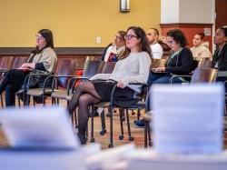 An audience of mostly women and one man sit, listening to a speaker.