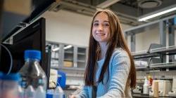 A female student smiles at a computer in a science lab.