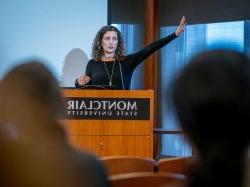 A professor gestures while speaking at a lectern.